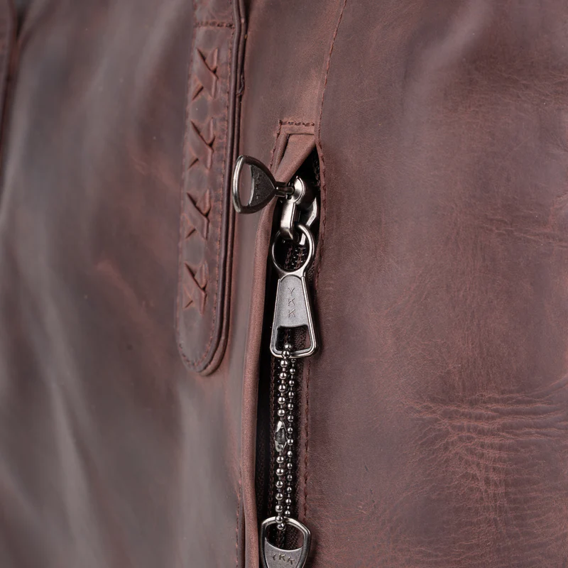 Close-up of Norah tote locking zipper hardware showing lockable YKK zipper pull and leather flap detail